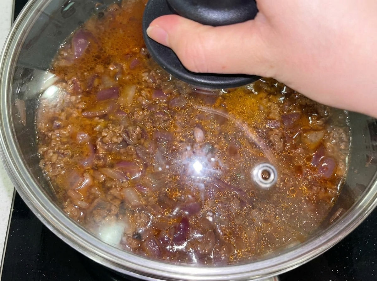 Rindfleisch-Zwiebel-Mischung in einer abgedeckten Pfanne mit Glasdeckel, nachdem Wasser hinzugefügt wurde.