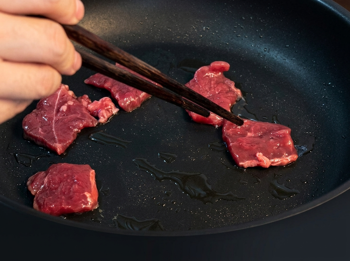 Dünne Rindfleischstreifen werden in einer heißen, geölten Pfanne angebraten und bräunen beim Garen.