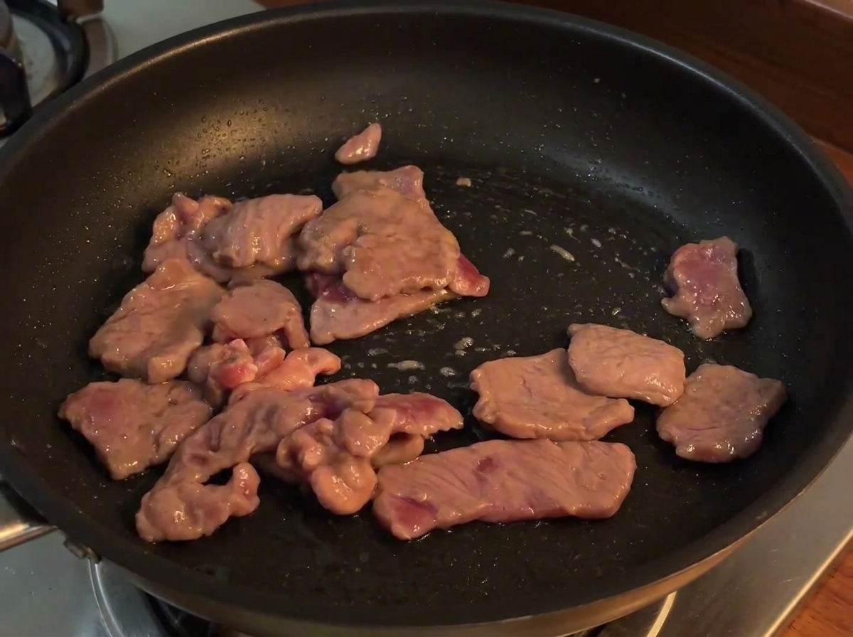 Geschnittene rote Zwiebeln werden zum gegarten Rindfleisch in die Pfanne gegeben und mitgebraten.