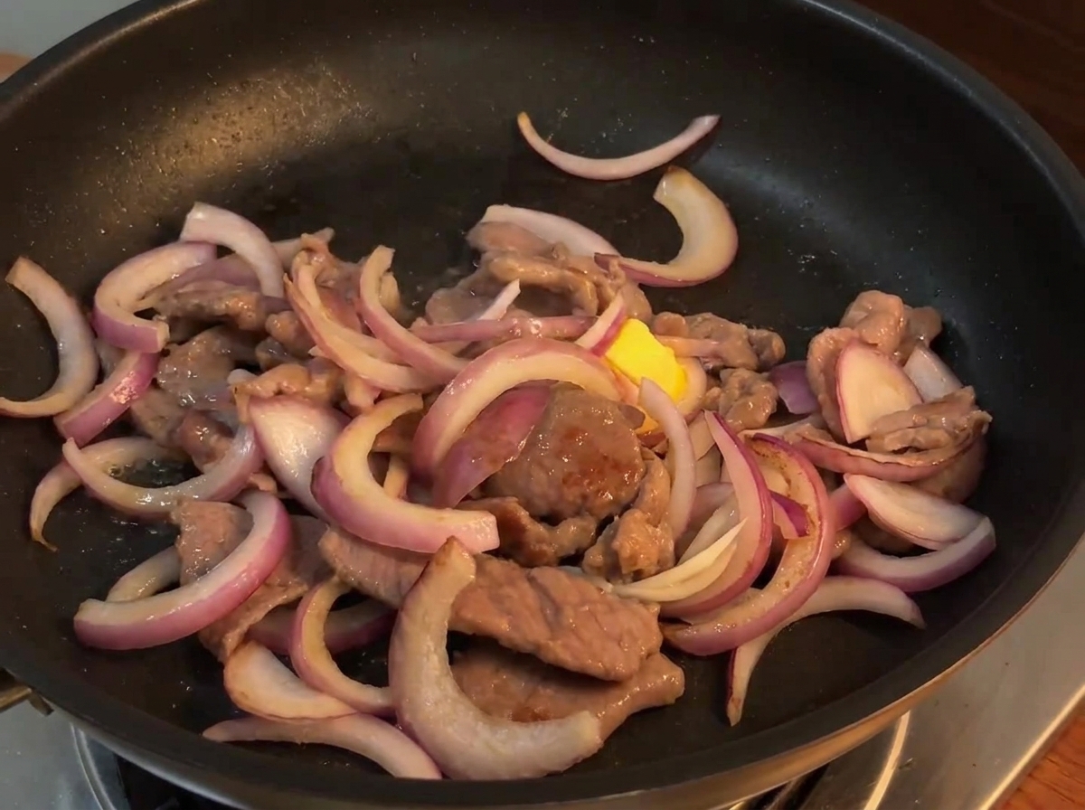 Die Pfannensauce wird aus einer kleinen Schüssel über die Rindfleisch-Zwiebel-Mischung in der heißen Pfanne gegossen.