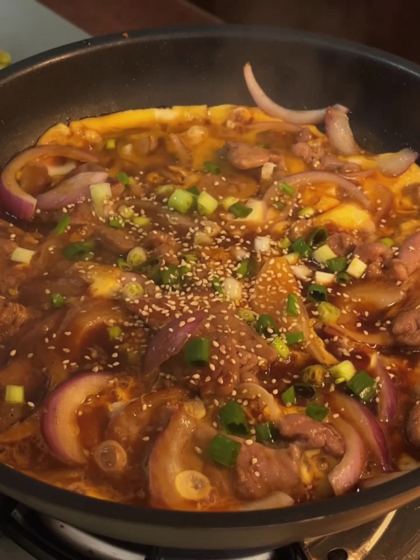 Ein fertiges Rindfleisch-Ei-Gericht in einer Pfanne, garniert mit frischen gehackten Frühlingszwiebeln und geröstetem Sesam.