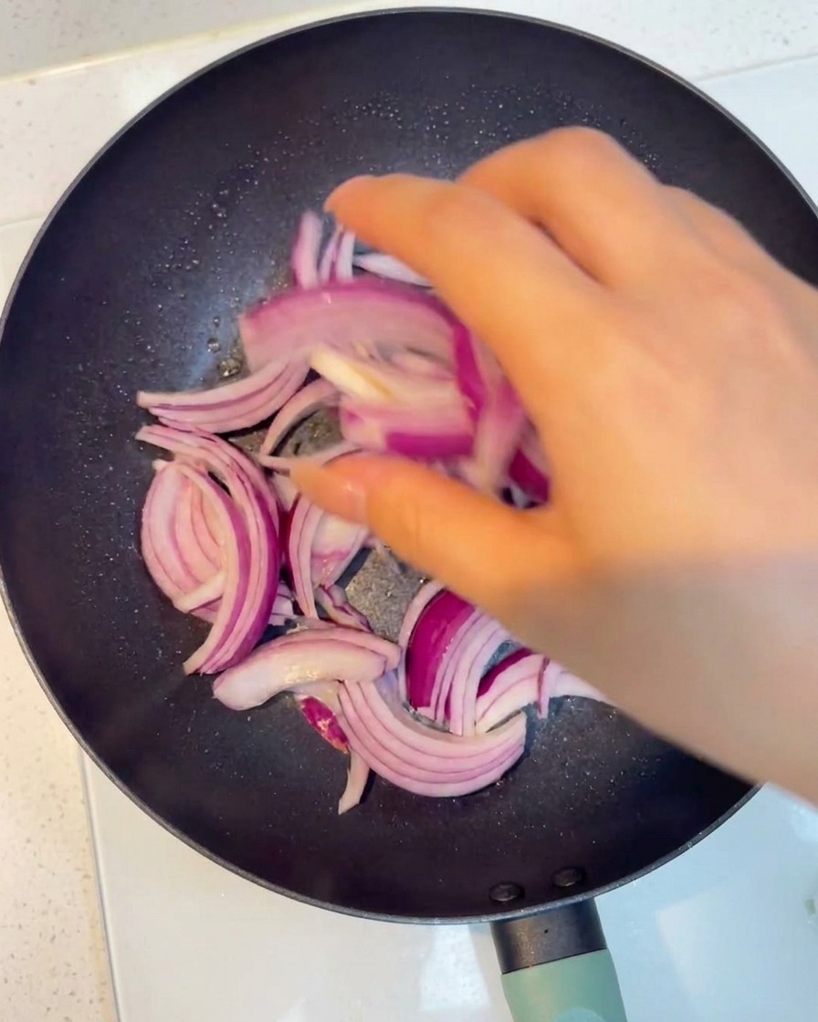 Rote Zwiebelstreifen werden in der Pfanne glasig gedünstet.