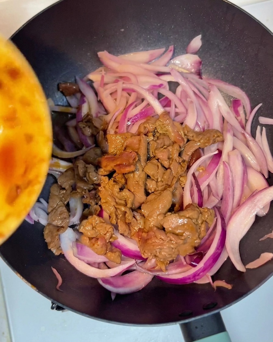 Gebratenes Rindfleisch wird zu den Zwiebeln in die Pfanne gegeben.