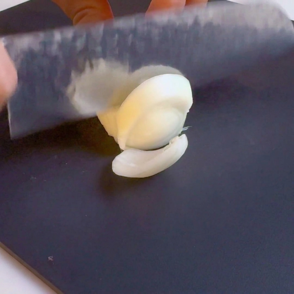 Ein Messer, das eine weiße Zwiebel auf einem schwarzen Schneidebrett in Streifen schneidet.