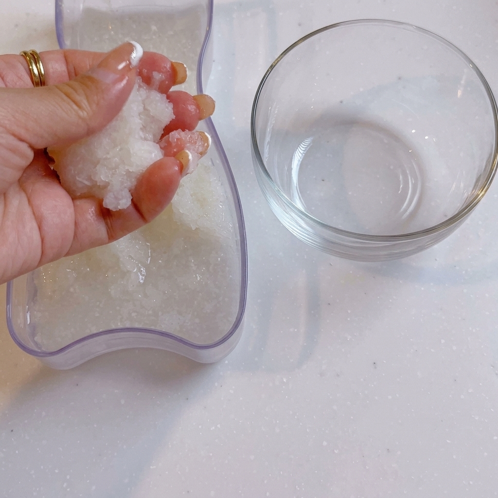 Eine Hand drückt Wasser aus dem geriebenen Daikon-Rettich neben einer durchsichtigen Glasschüssel.