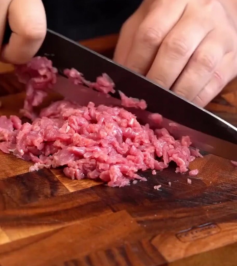 Fein gehacktes, frisches Rindfleisch auf einem Holzbrett, bereit zur weiteren Verarbeitung.