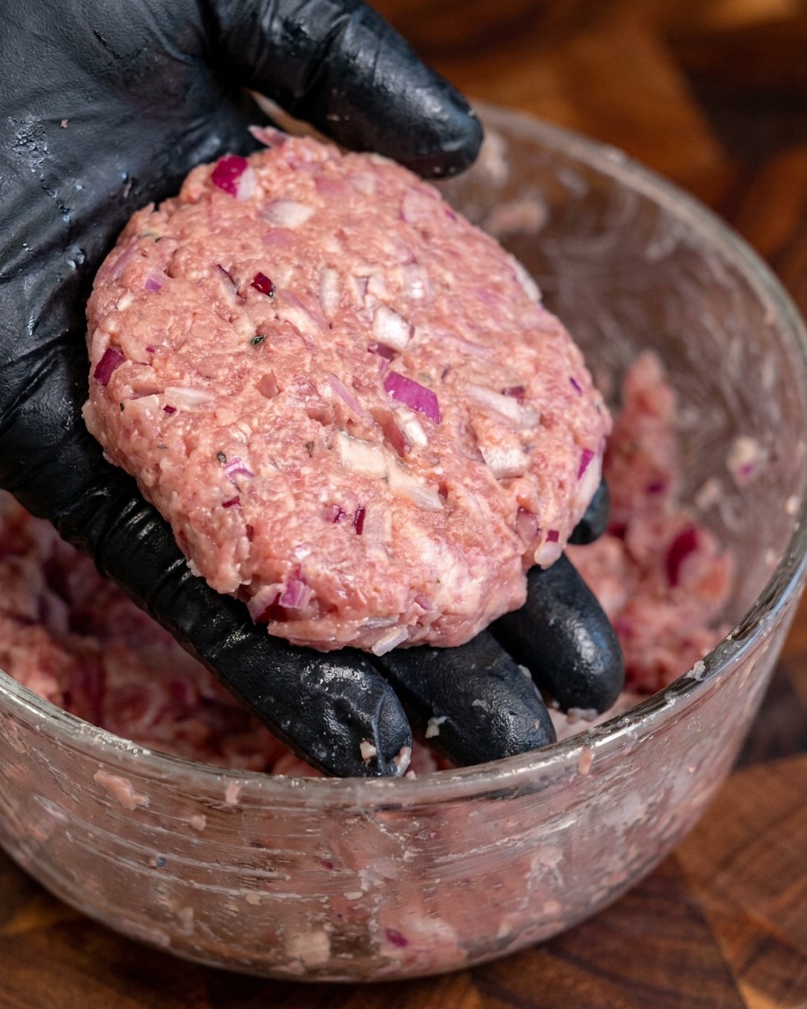 Mehrere dicke, handgeformte, gewürzte Rinder-Patties.