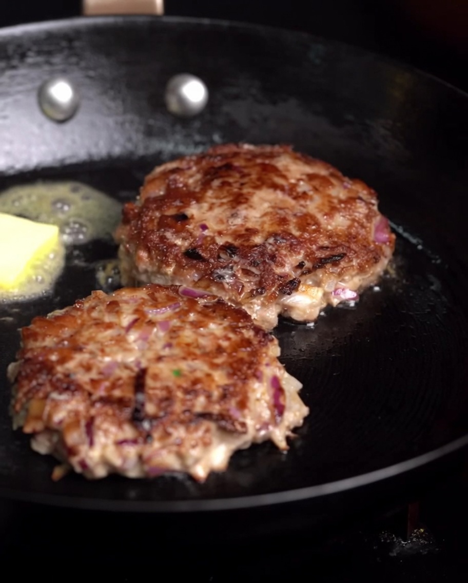 Patties in der Pfanne, während Butter schmilzt und ein Zweig Rosmarin dazugegeben wird.