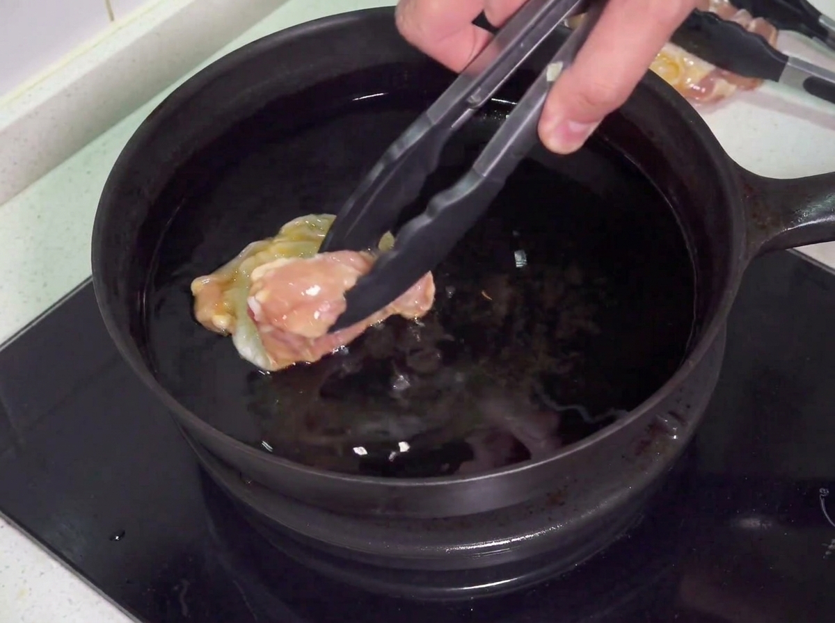 Rohe Hähnchenkeulen werden vorsichtig in eine Pfanne mit heißem Öl zum Frittieren gelegt.