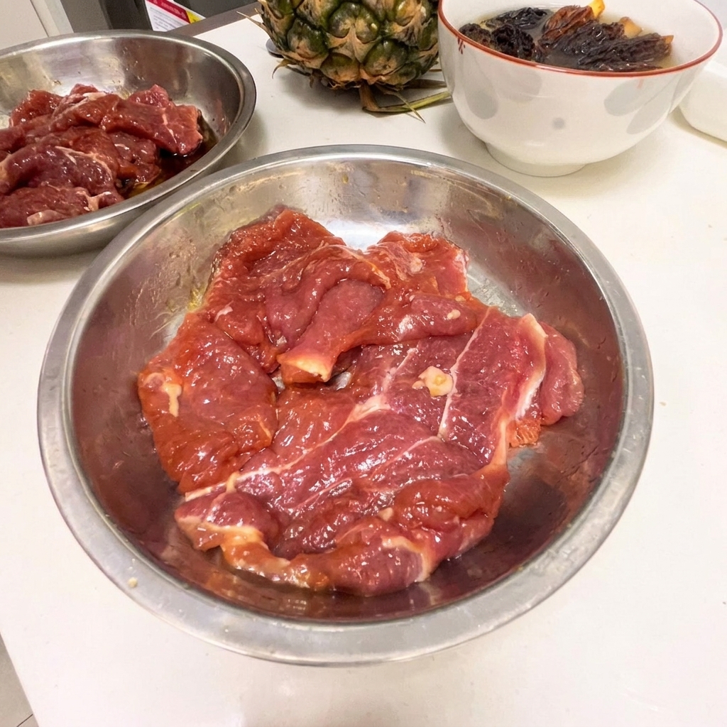 Dünne Scheiben roher Schweinenacken in einer Edelstahlschüssel mit dunkler Marinade.