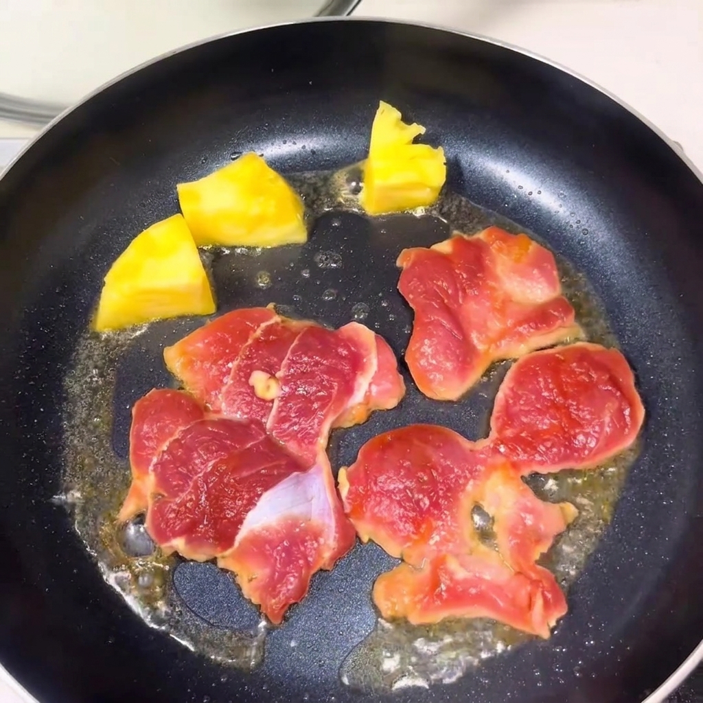 Fleischstücke und Ananasstücke braten zusammen in der Pfanne.