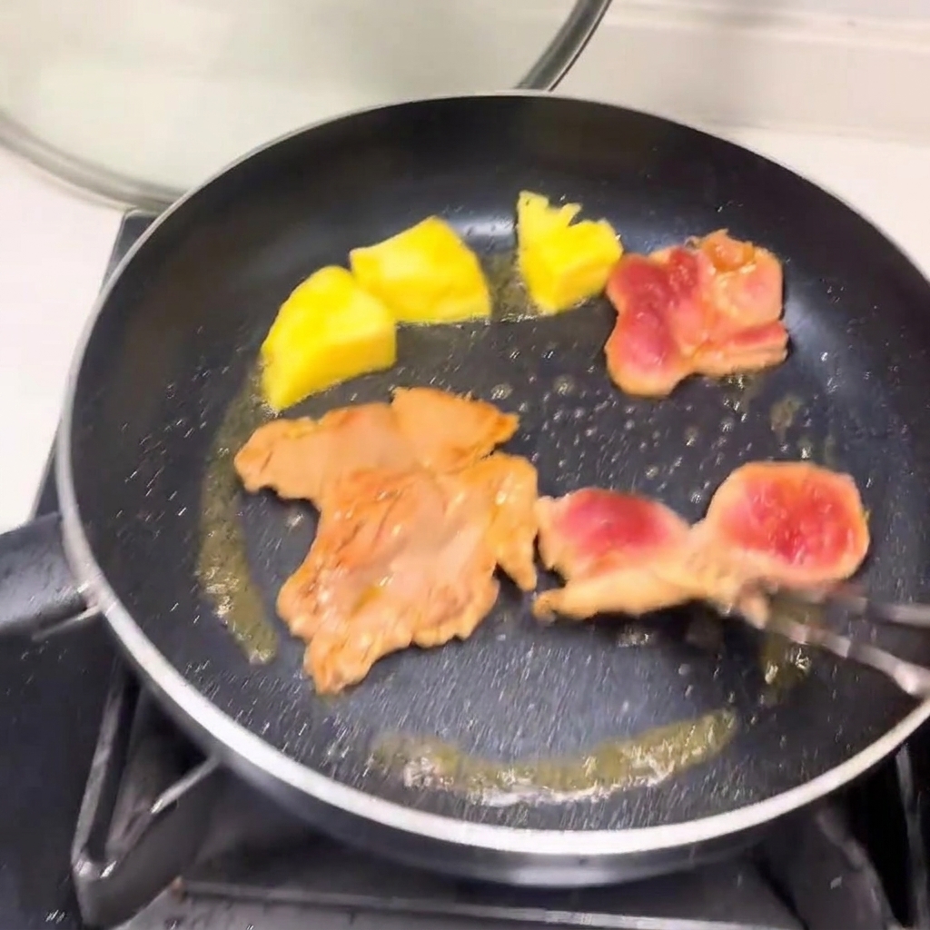 Gebräunte Fleischstücke und Ananas in der Pfanne.