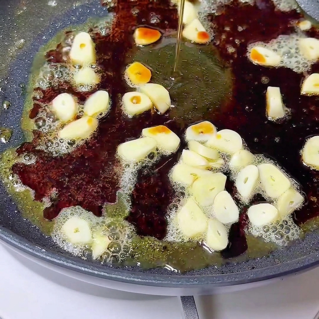 Flüssigkeit wird über geschnittenen Knoblauch und geschmolzene Butter in einer dunklen Pfanne gegossen.