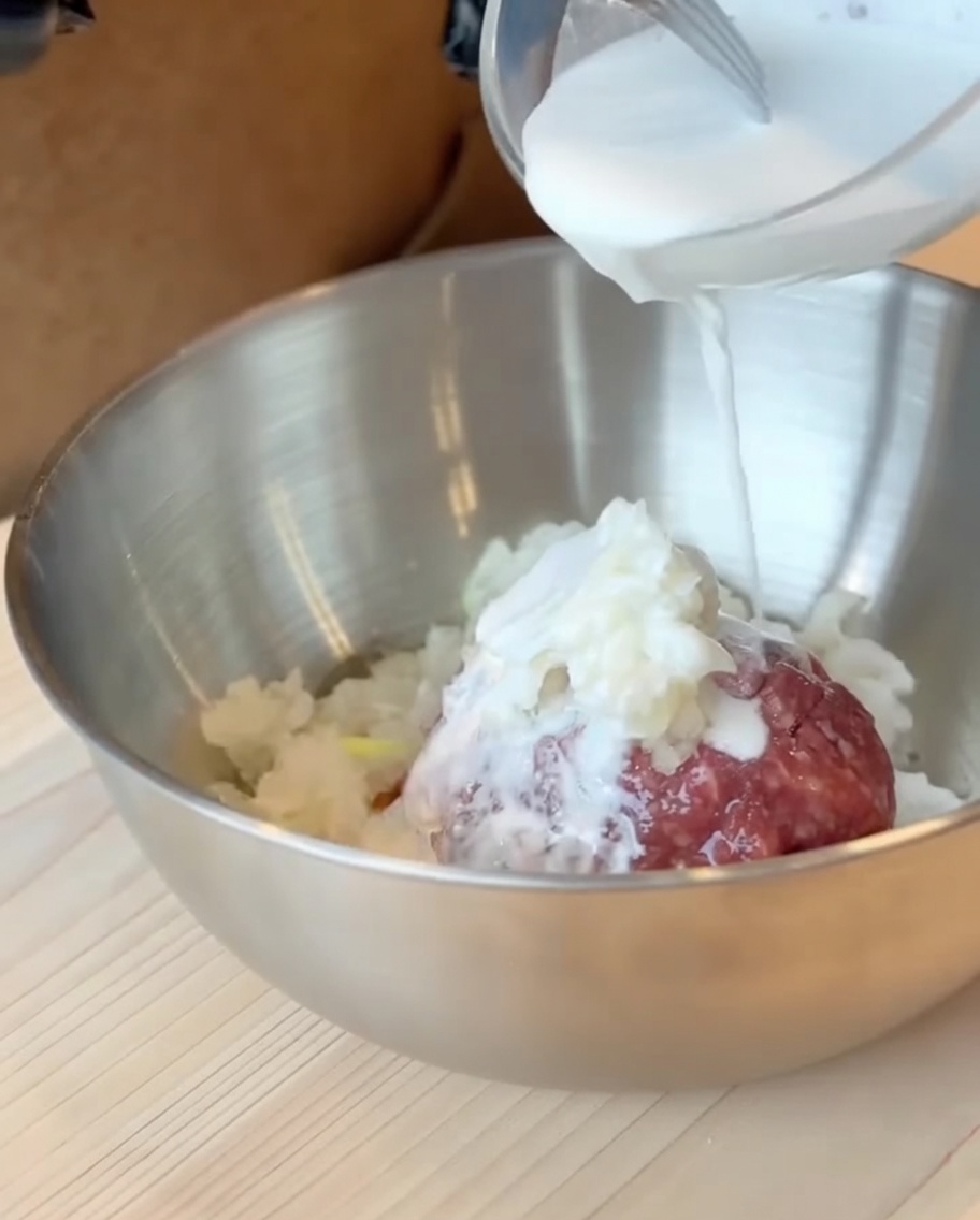 Die Mischung aus Milch und Süßkartoffelmehl wird über das Rinderhackfleisch in einer großen Schüssel gegossen.