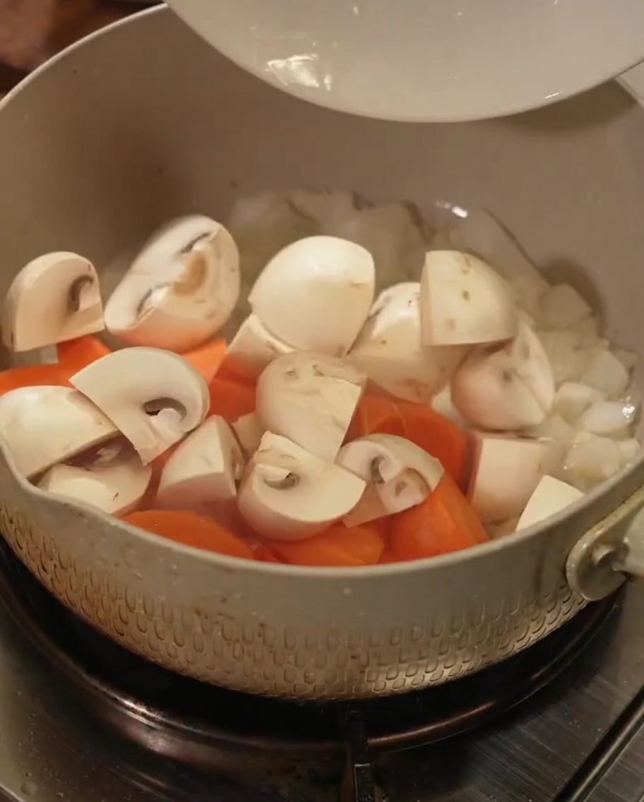 Karottenstücke und geschnittene Pilze in einem Kochtopf.