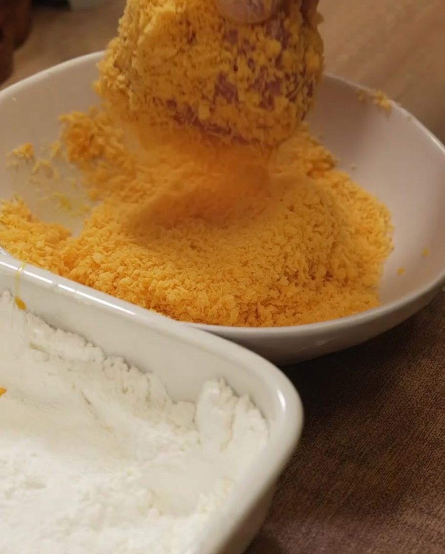 Hähnchenbrust wird fest in eine Schüssel mit goldenem Paniermehl gedrückt.
