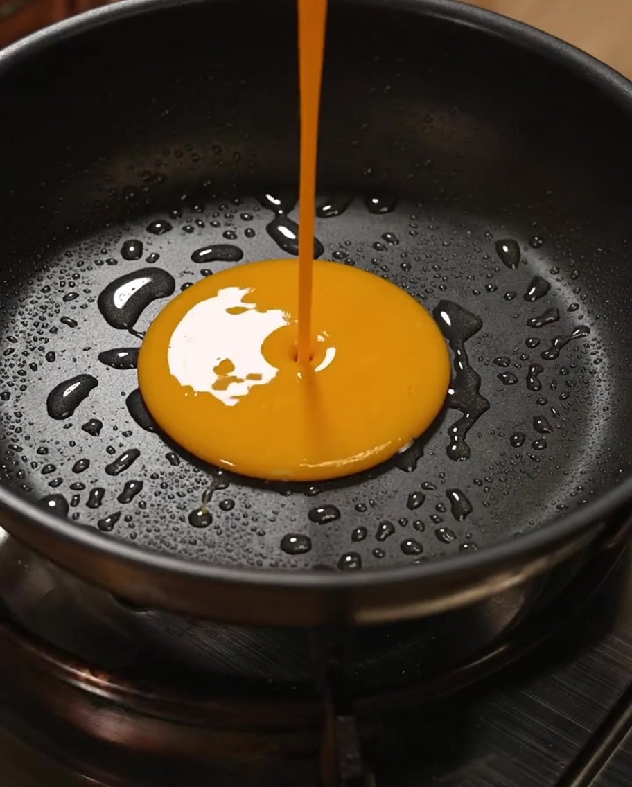 Goldene Eiermasse wird in einer Pfanne zu weichem Rührei gerührt.