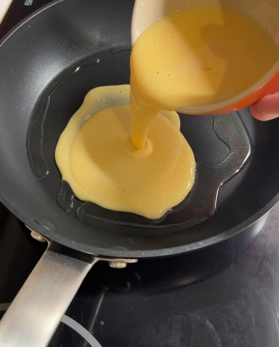 Eine gelbe Ei-Milch-Mischung, die in eine heiße Pfanne gegossen wird, bereit zum Rühren.