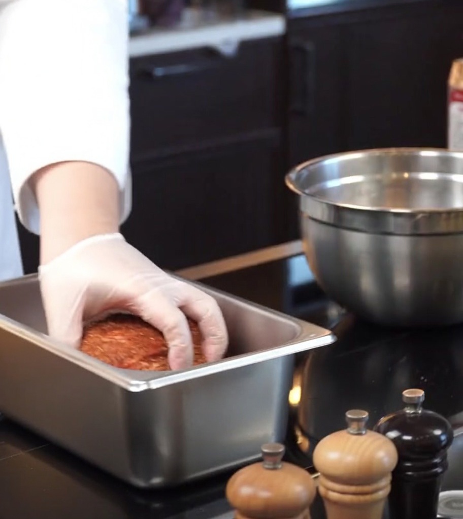 Das gewürzte Fleisch wird in eine rechteckige Backform aus Edelstahl gelegt.