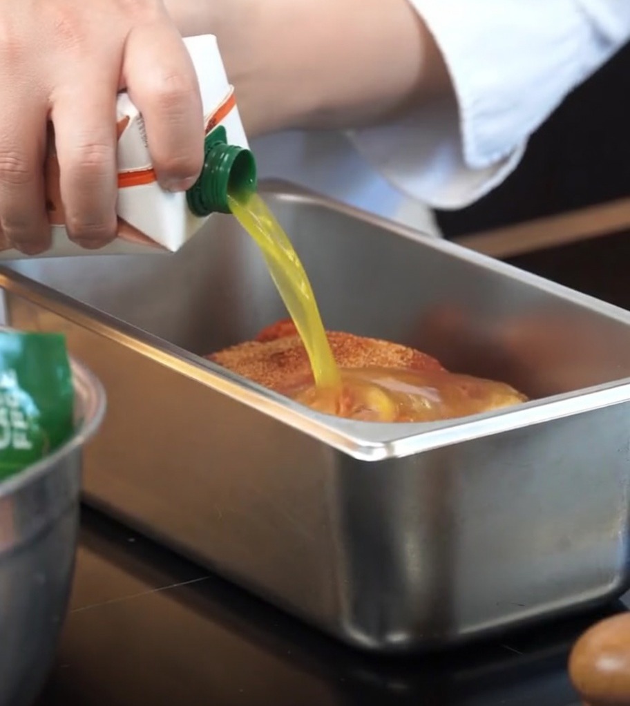 Orangensaft wird aus einem Karton in die Backform zum Fleisch gegossen.