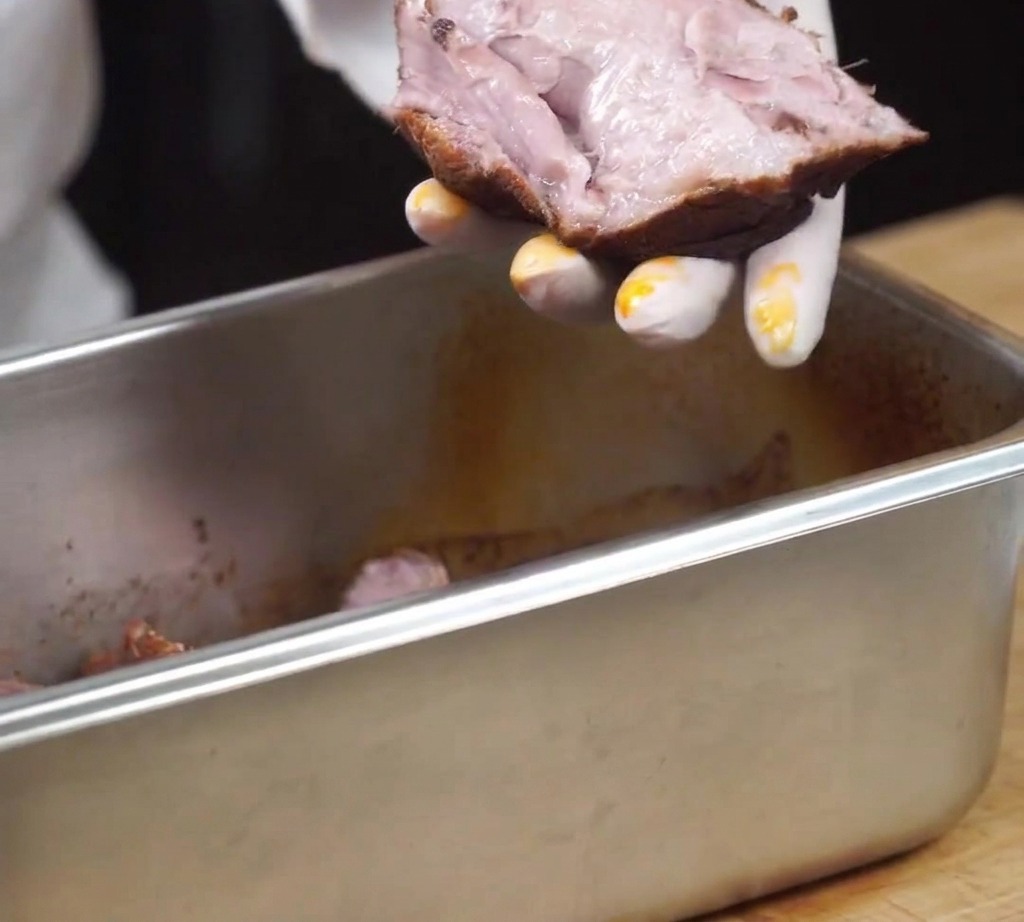 Ein Stück gegartes Schweinefleisch wird mit den Händen in Fasern gezupft.