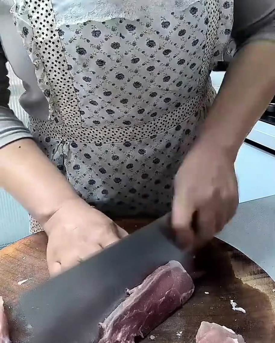 Ein scharfes Messer schneidet rohes Schweinefleisch auf einem Holzbrett.