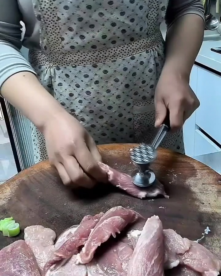Ein Fleischhammer bearbeitet Schweinefleischstücke auf einem Holzbrett.