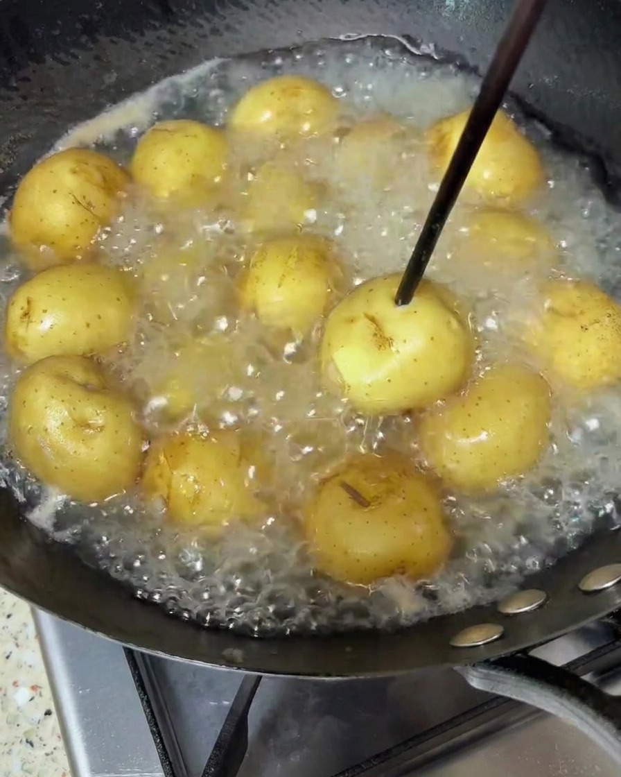 Babykartoffeln köcheln in kochendem Wasser, ein Holzstäbchen prüft die Garstufe.
