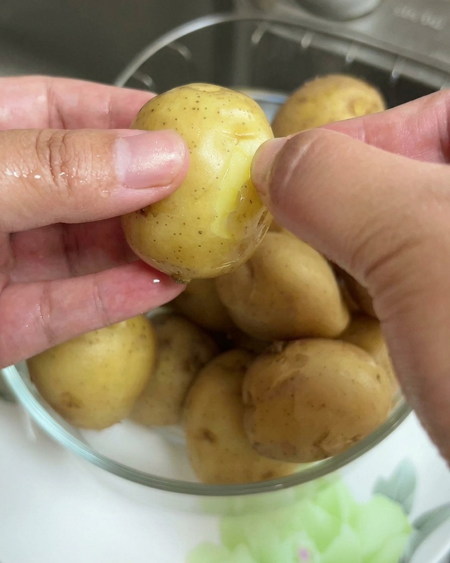 Nahaufnahme von Händen, die die dünne Haut von einer gekochten Babykartoffel abziehen.