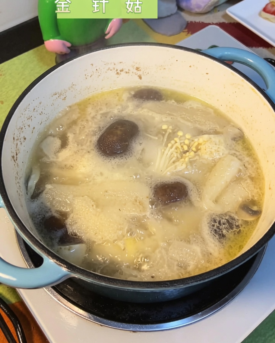 Enoki-Pilze werden in die sprudelnde Hähnchen-Pilz-Brühe getaucht.