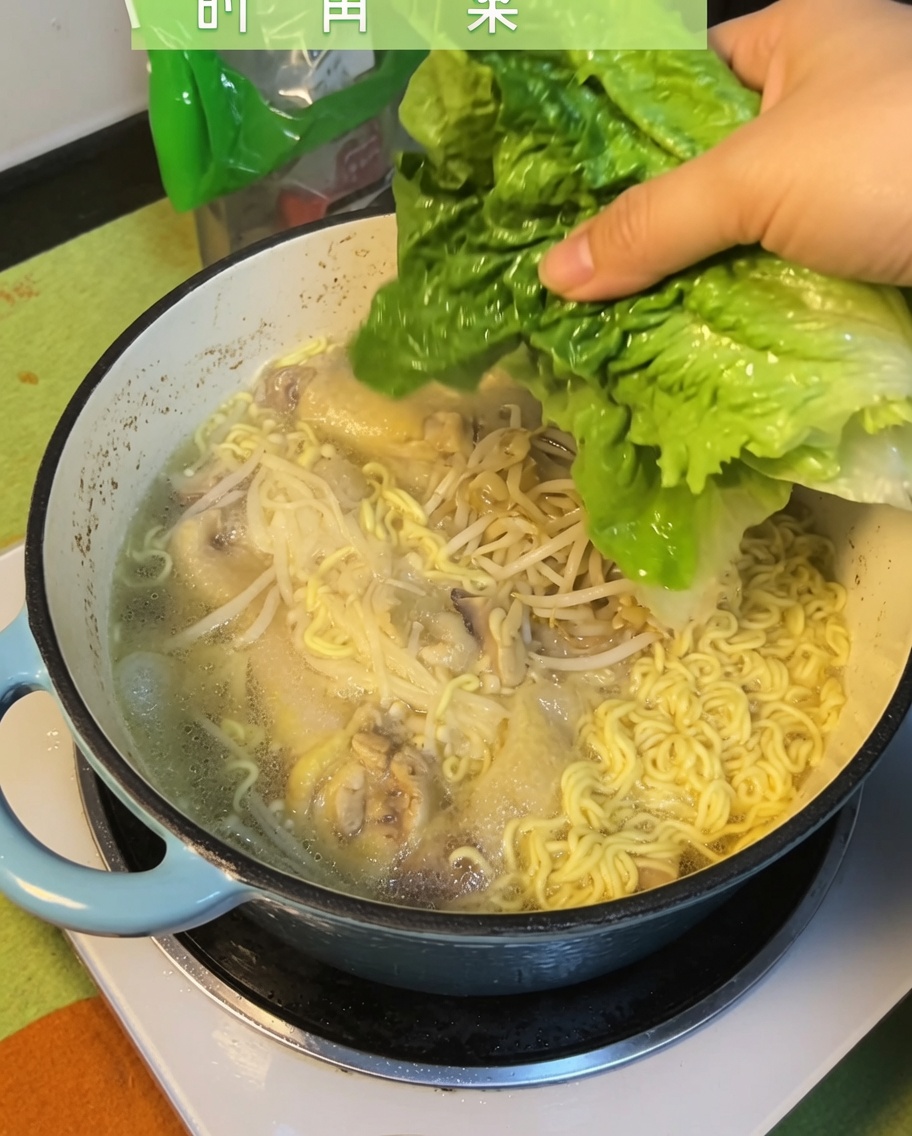 Frische grüne Pak-Choi-Blätter werden in die fertige Hähnchen-Nudelsuppe gegeben.