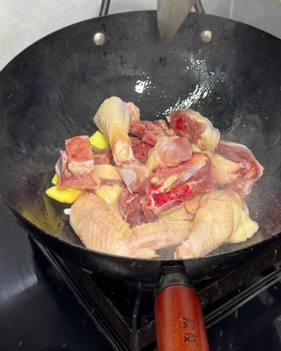 Frische Hühnerstücke werden mit Ingwerscheiben in einem Wok angebraten.