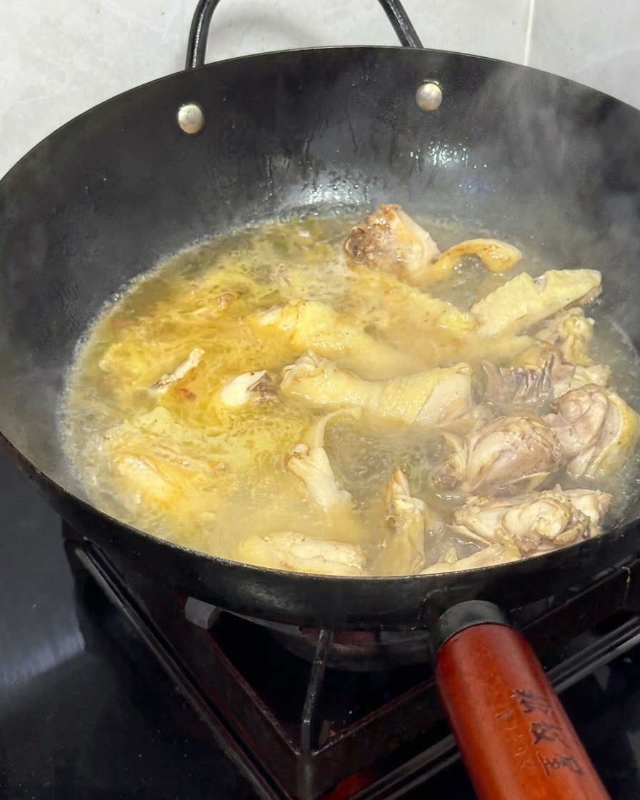 Heißes Wasser wird in den Wok zu dem angebratenen Huhn und Ingwer gegossen.
