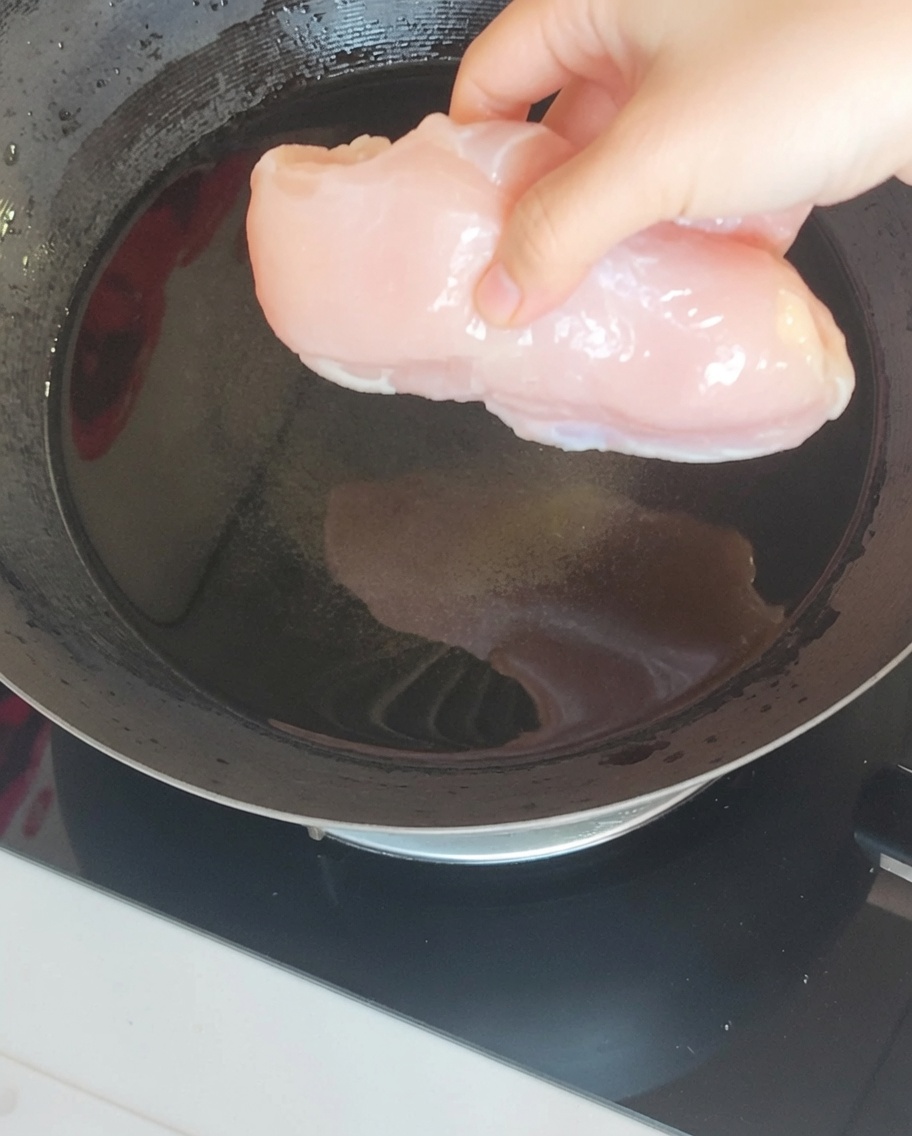 Eine Hähnchenbrust kocht in einem Wok mit Ingwer und Frühlingszwiebeln.