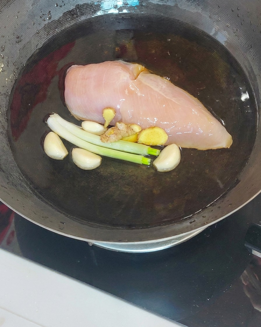 Gekochte Hähnchenbrust wird mit einem Schaumlöffel aus dem Wok gehoben.