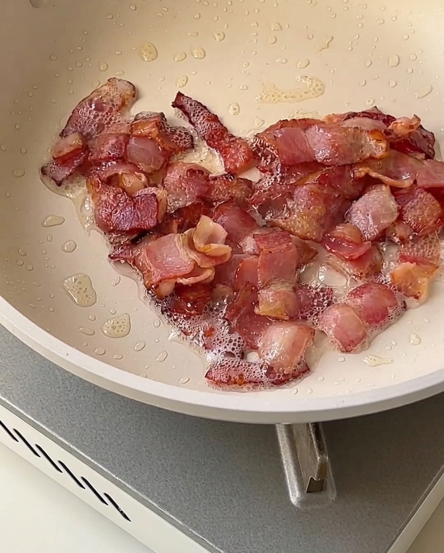 Zwiebel-, Sellerie- und Kartoffelwürfel, die in einer Pfanne zusammen mit knusprigen Speckstücken braten.