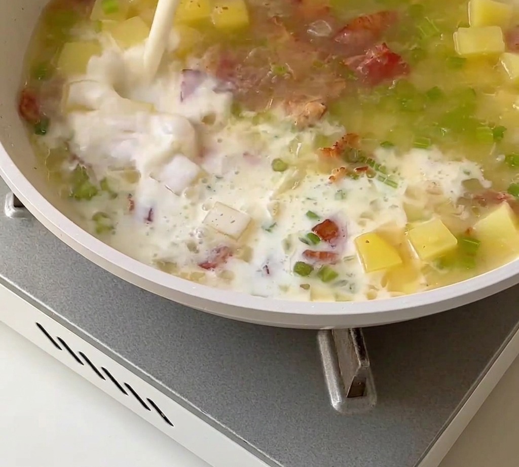 Eine cremige Muschelsuppenbasis, die mit Milch, Sahne und Muschelfleisch in einer Pfanne verrührt wird.