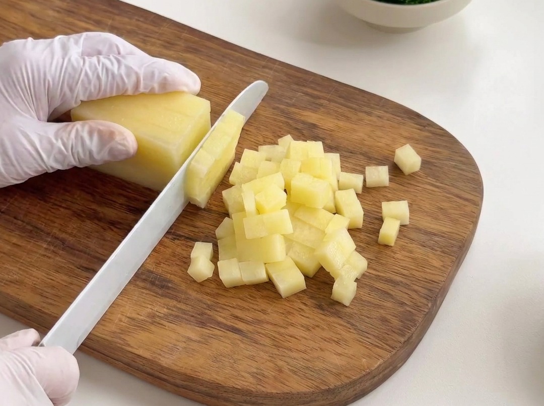 Geschälte Kartoffeln werden auf einem Holzbrett in kleine, gleichmäßige Würfel geschnitten.