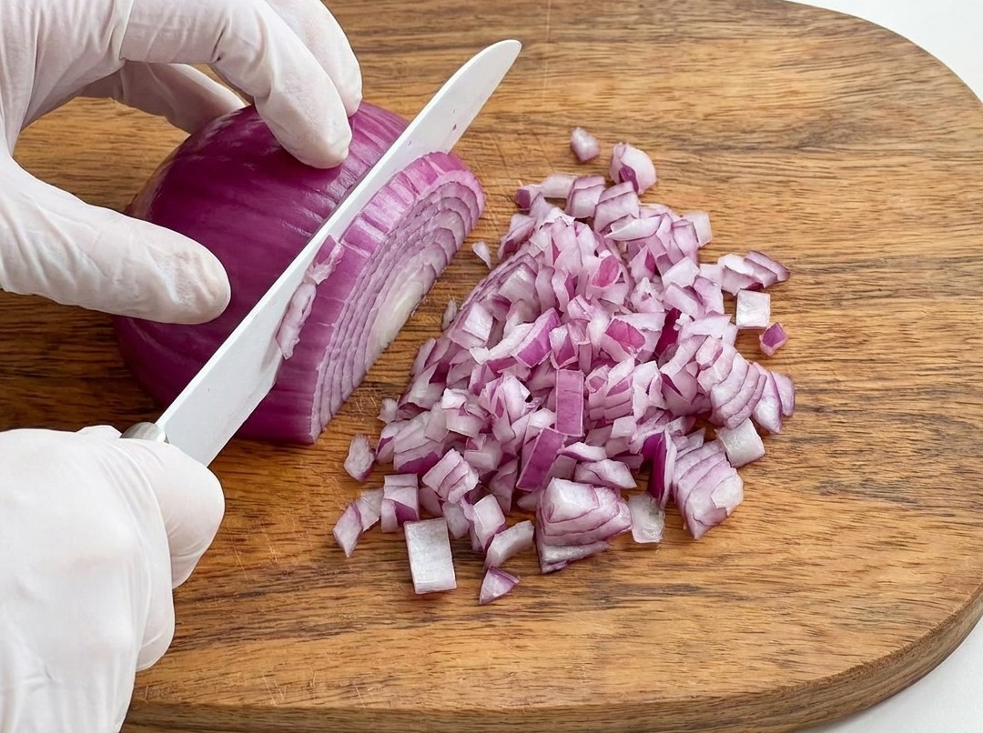 Rote Zwiebel wird auf einem Holzbrett fein gewürfelt.