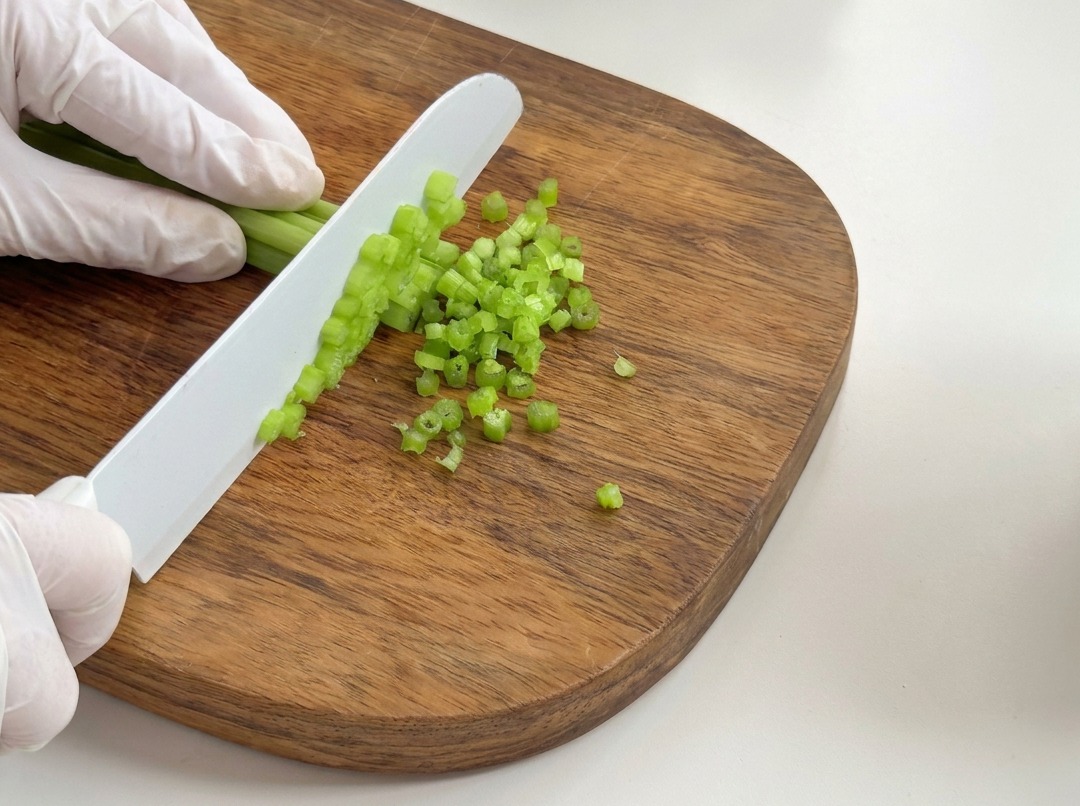 Frische Selleriestangen werden auf einem Holzbrett in kleine Stücke geschnitten.