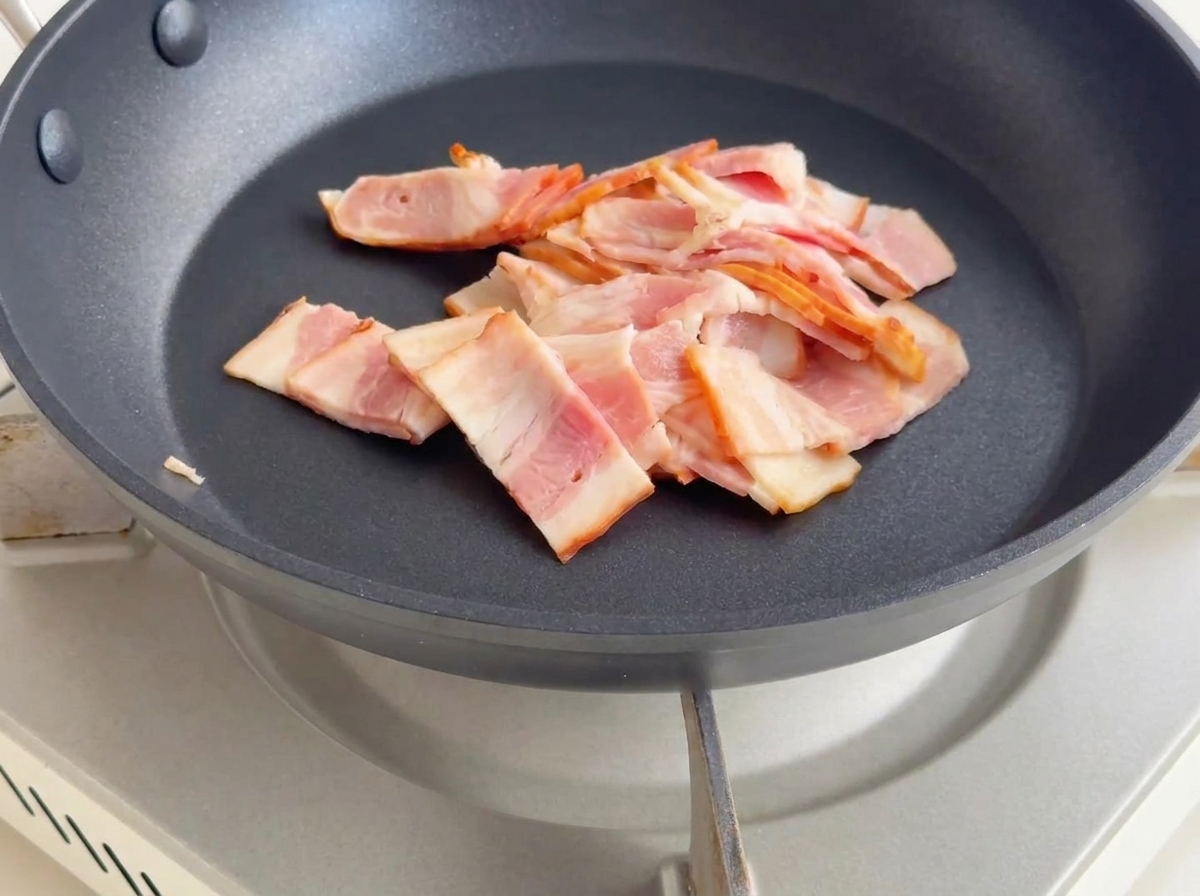 Kleine Speckwürfel braten in einer Pfanne, werden goldbraun und geben Fett ab.
