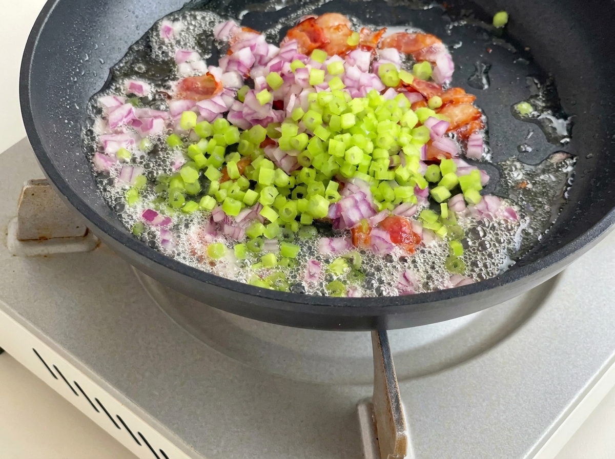 Gewürfelte Kartoffeln, Sellerie und rote Zwiebel werden zum Speck und Fett in die Pfanne gerührt.