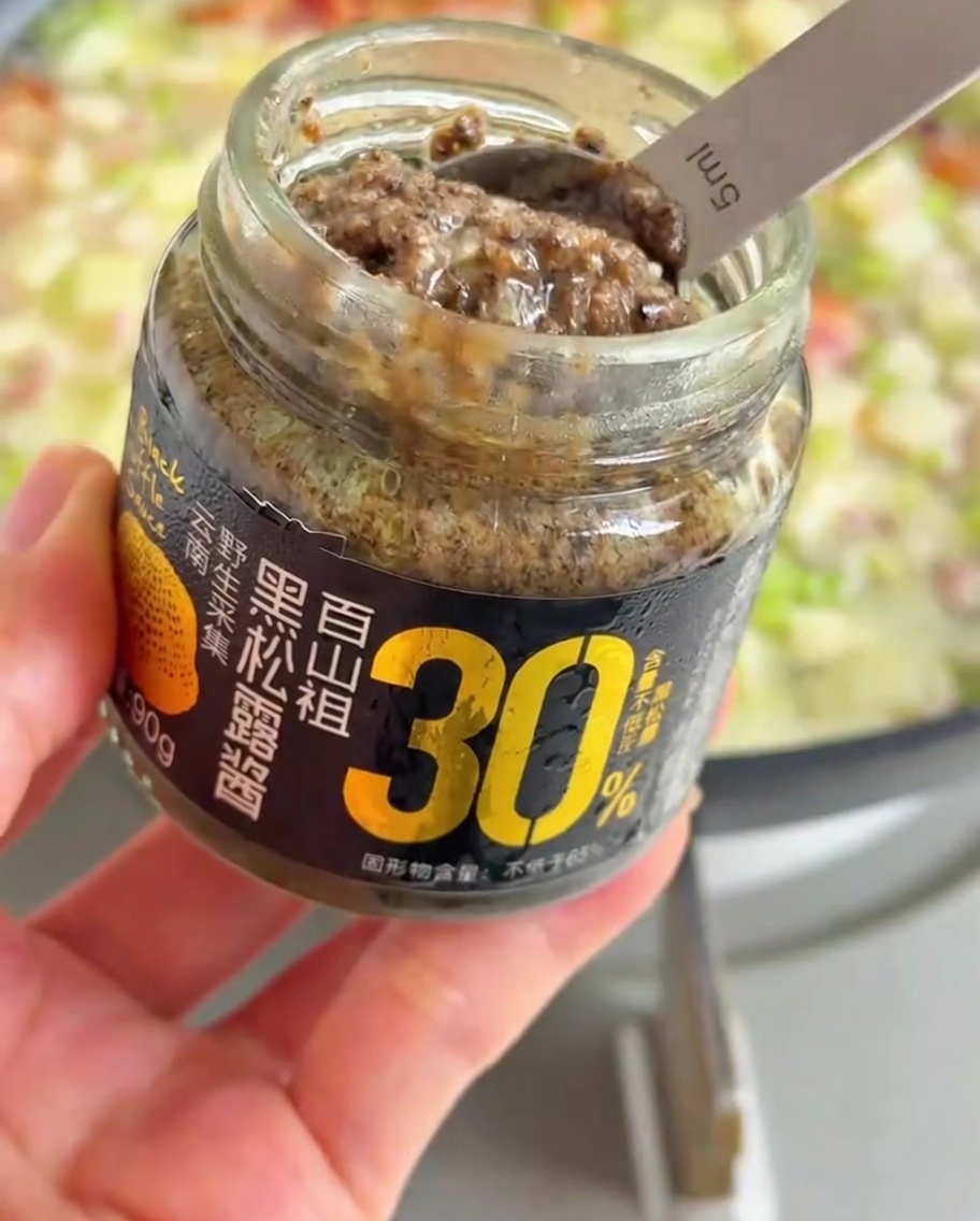 Ein Löffel dunkle schwarze Trüffelpaste wird zu der blubbernden Pfanne mit Gemüse und Brühe gegeben.