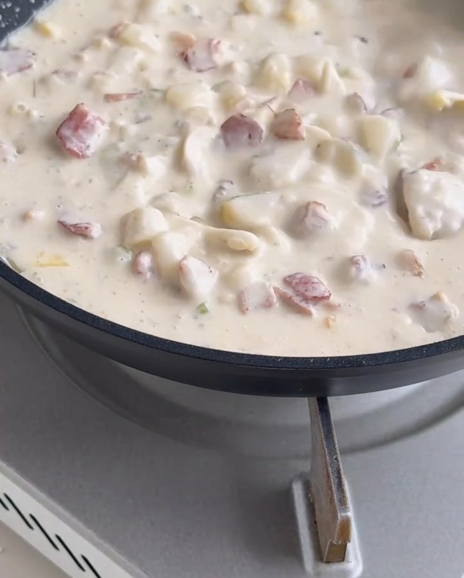Muschelfleisch wird in die cremige, blubbernde Suppe in der Pfanne gerührt.