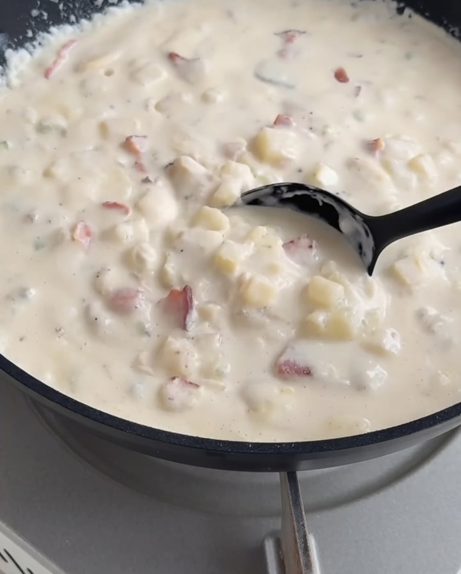 Cremige Clam Chowder wird aus einem Topf in einen vorbereiteten knusprigen Brotlaib geschöpft.