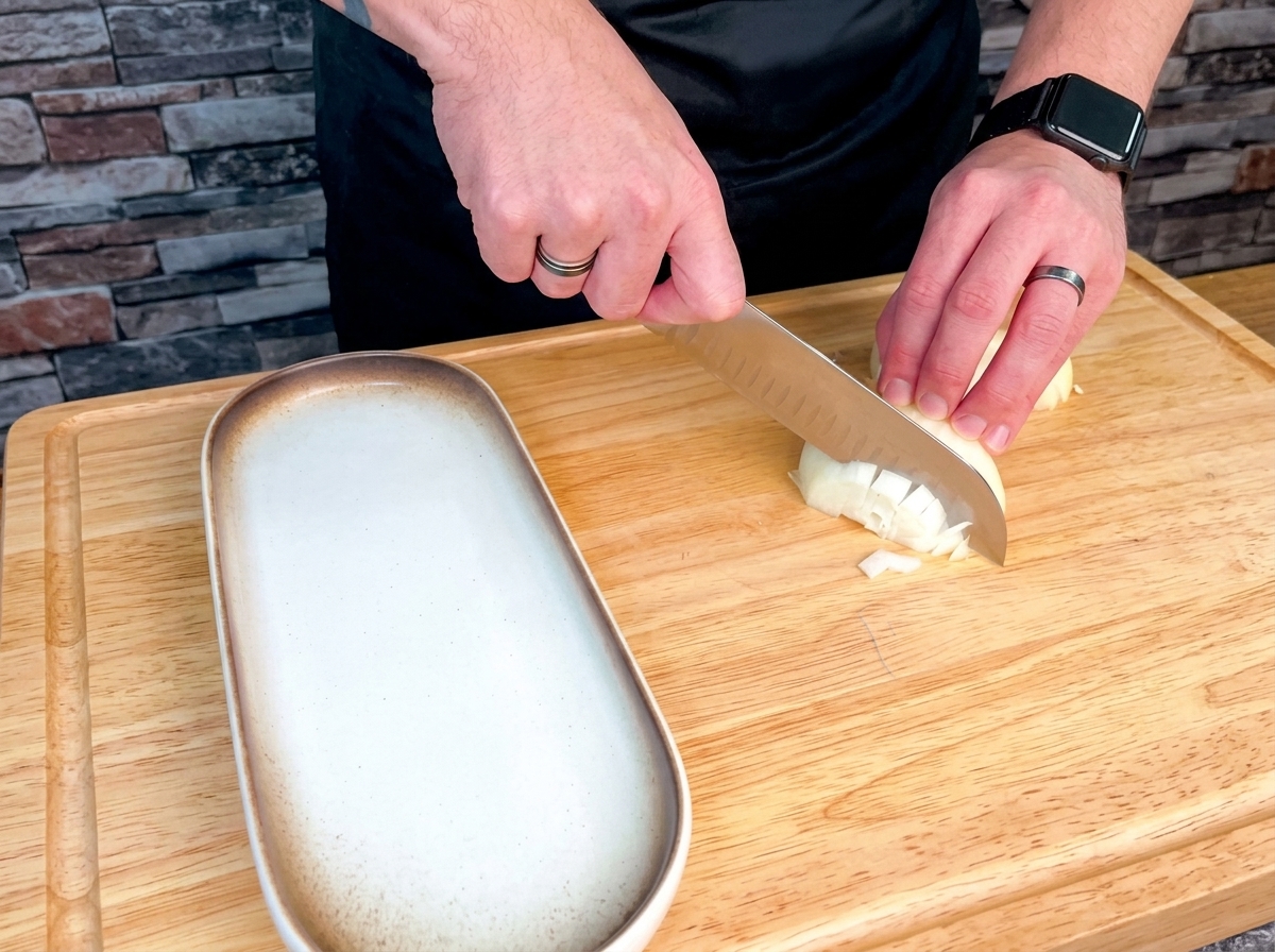 Eine Auswahl an frischem Gemüse, bestehend aus Zwiebeln, Sellerie, Karotten, Knoblauch und Kartoffeln, sauber gewürfelt auf einem großen Holzschneidebrett.