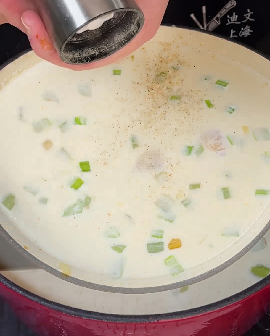 Lorbeerblatt und frischer Thymian werden einem köchelnden Topf mit cremiger Clam Chowder hinzugefügt.