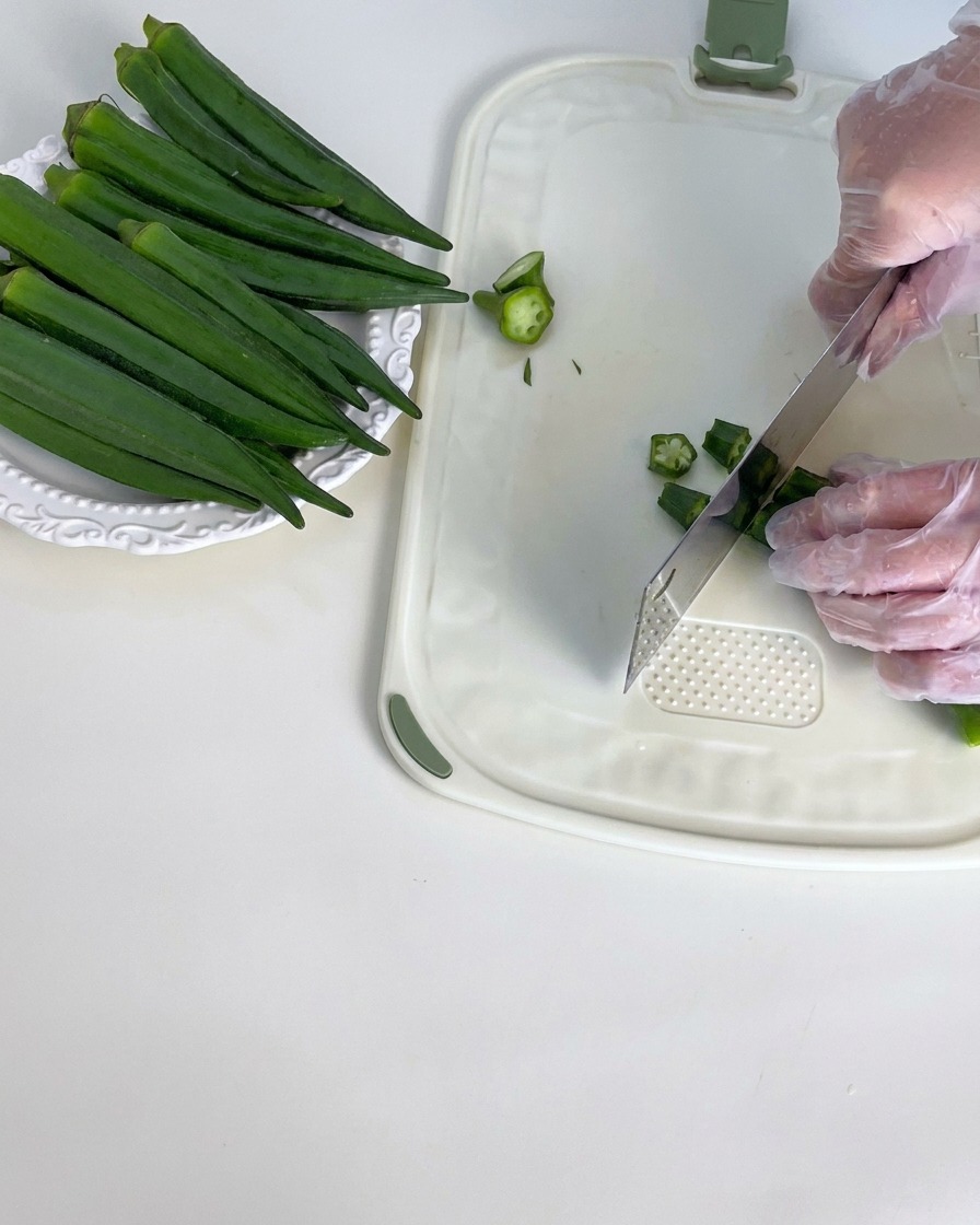 Frische grüne Okraschoten werden auf einem weißen Schneidebrett von den Stielenden befreit.