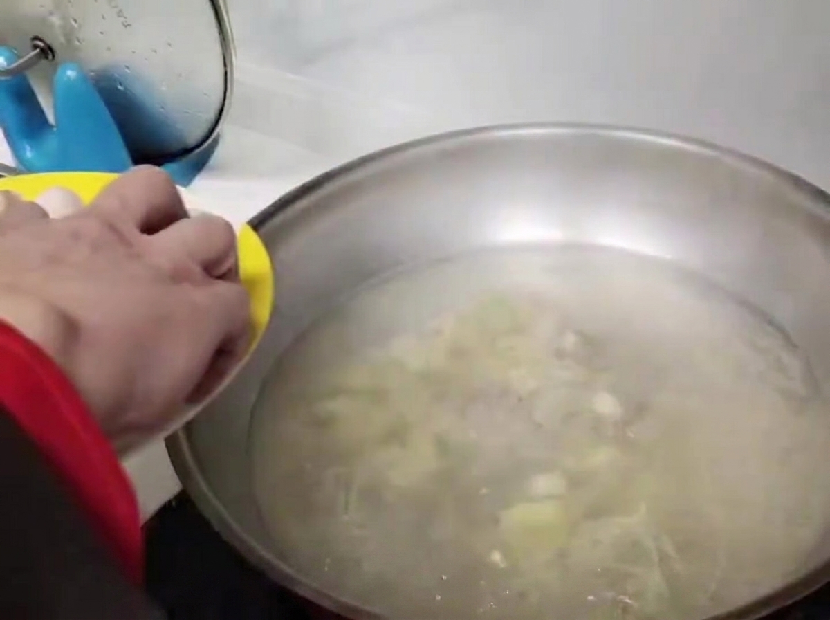 Runde Fleischbällchen werden vorsichtig in das kochende Wasser in einem Edelstahl-Wok gegeben.
