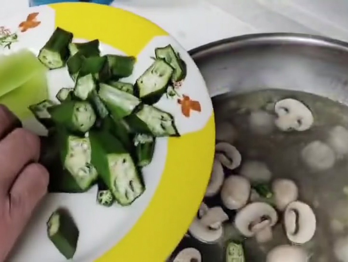 Frisch geschnittene Pilze und Okra-Segmente werden in die köchelnde Fleischbällchensuppe gegeben.